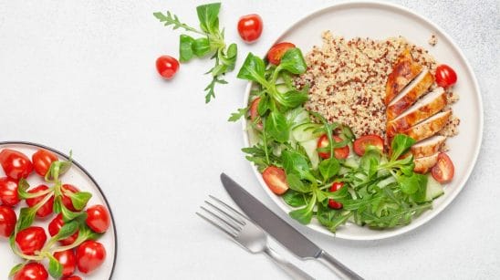 Chicken, salad, quinoa, and tomatoes on a dinner plate with white background